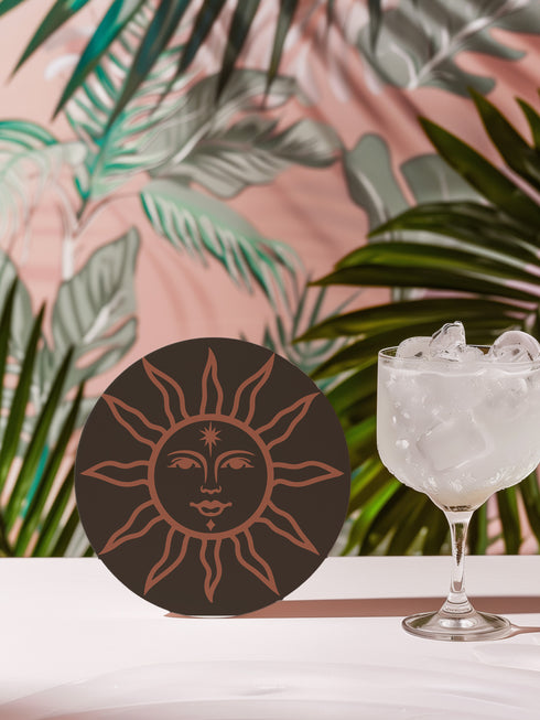 Round ceramic coaster in deep black featuring an intricate burnt-orange sun illustration with a serene, symmetrical face, radiating curved rays, and a delicate star detail on the forehead. The smooth, matte surface enhances the contrast between the dark background and the warm-toned design, creating a celestial, vintage-inspired aesthetic.